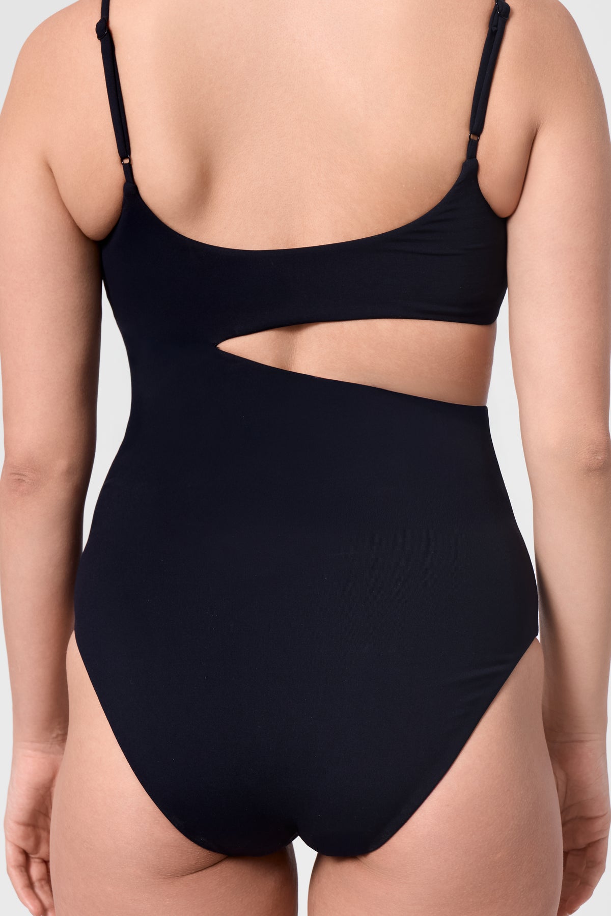 Model wearing the ROEM Nerissa One-Piece in Black, detail view highlighting the sculpted waist cutout